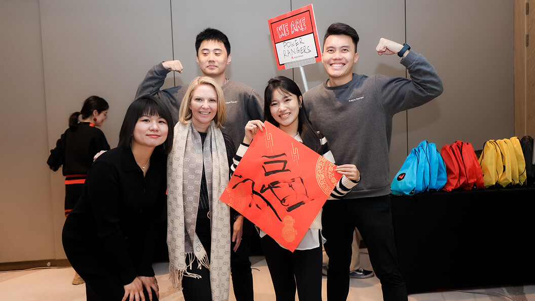 Five people pose and smile for a group photo indoors, holding a red sign with Chinese characters and another sign that says We Are Power Rangers. Colorful bags are visible on a table in the background.
